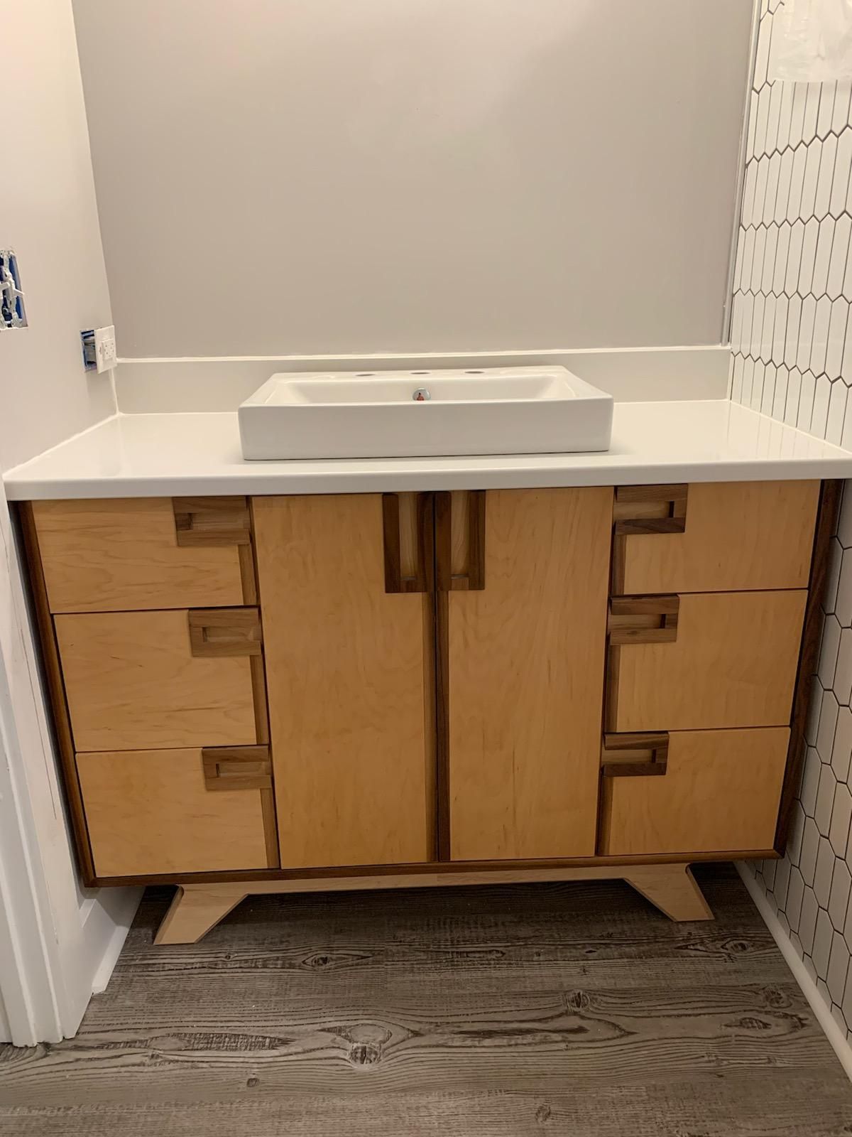 bathroom vanity with white stone top. Vanity body made from maple with walnut edge trim and handles